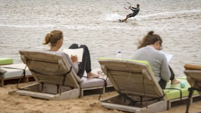 Deux vacanciers européens profitant du soleil à Dakhla, avec un touriste en train de faire du kitesurf dans les eaux atlantiques