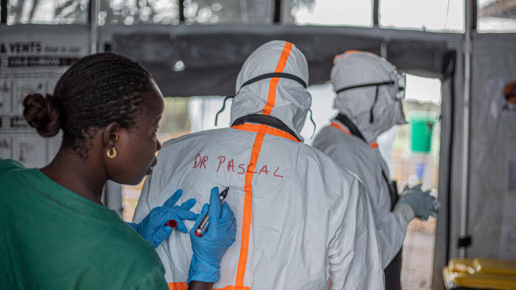Un agent de santé en tenue de protection individuelle (EPI) inscrit le nom d'un collègue avant d'entrer dans un centre de traitement Ebola (CTE) situé à Rwampara, à Bunia dans la province de l'Ituri, en RDC, le 13 juillet 2026.