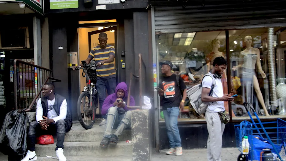 Un groupe de migrants debout devant un bâtiment administratif, visages floutés pour protéger leur identité